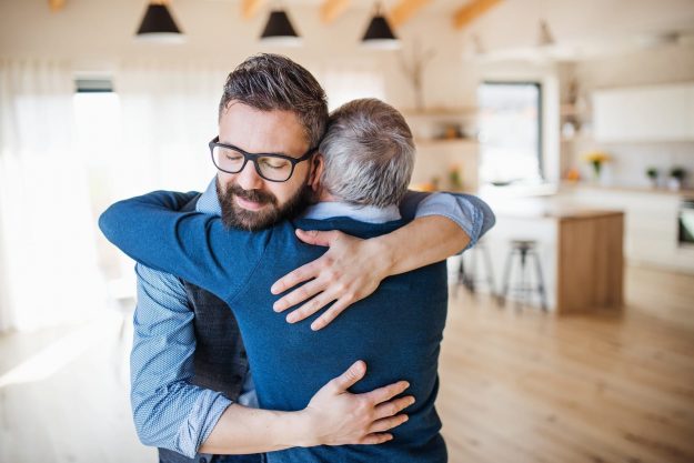 adult son and elderly father hug