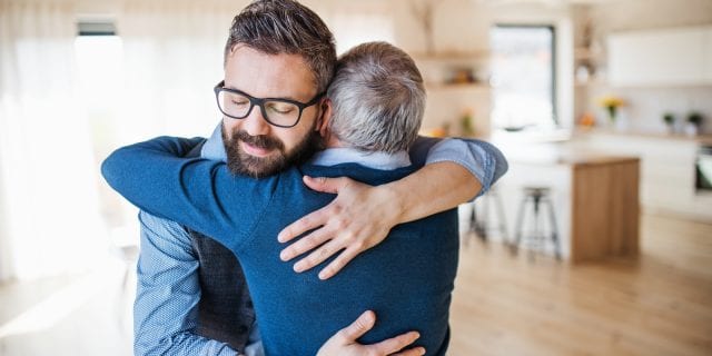 adult son and elderly father hug