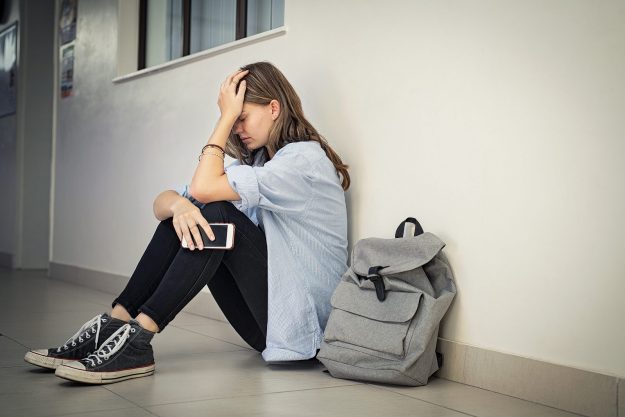 Upset and depressed girl holding smartphone sitting on college c