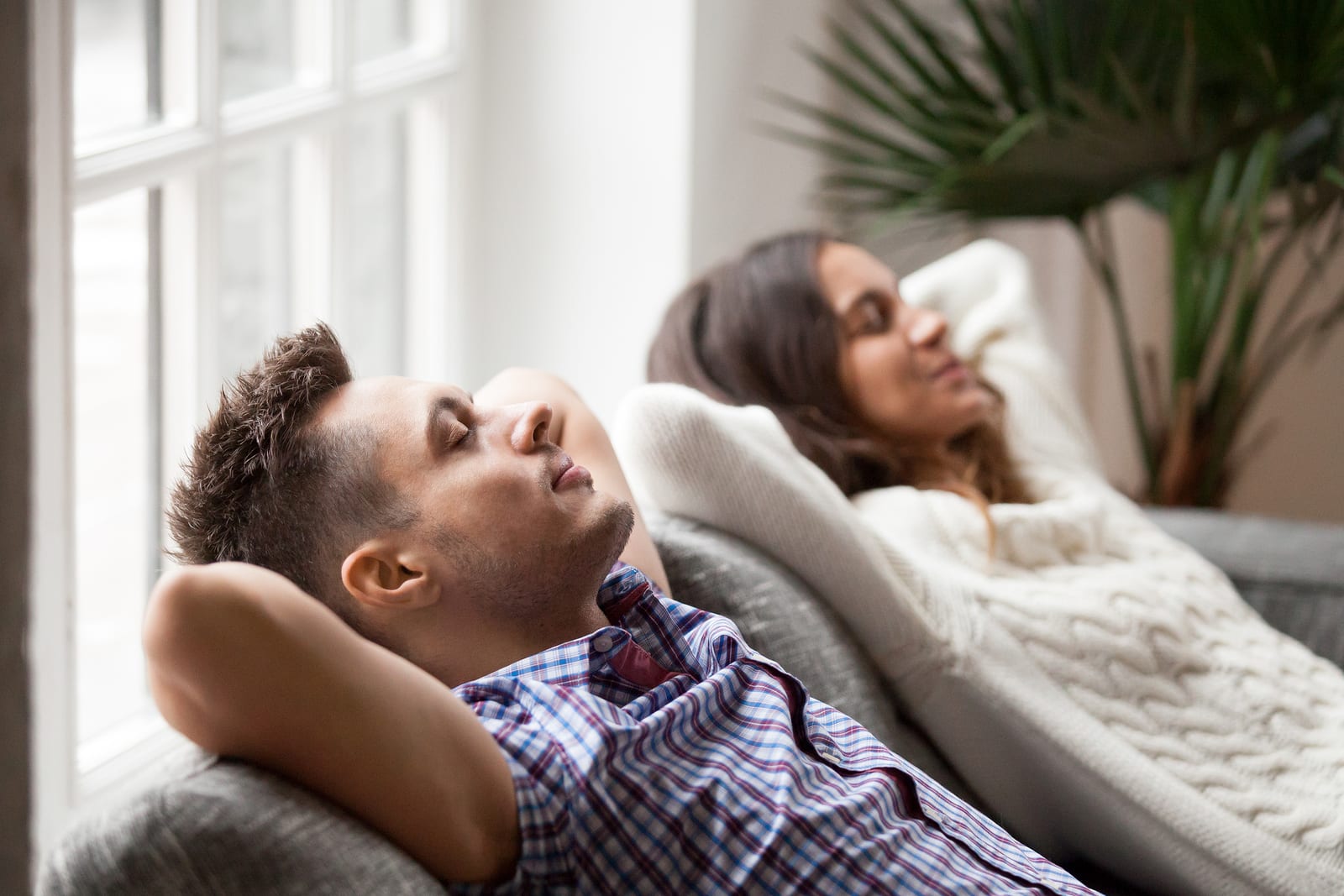 A young couple relaxes at home on the couch while deep breathing to reduce stress and anxiety.