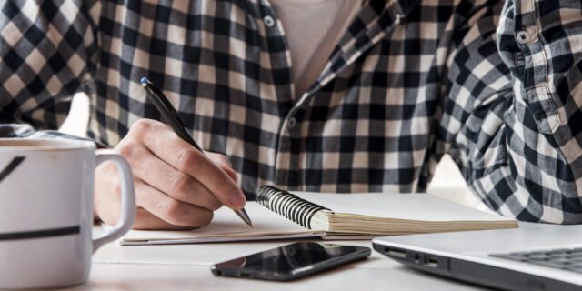 A man in a checkered shirt writing New Year's resolutions for his mental health in a notebook