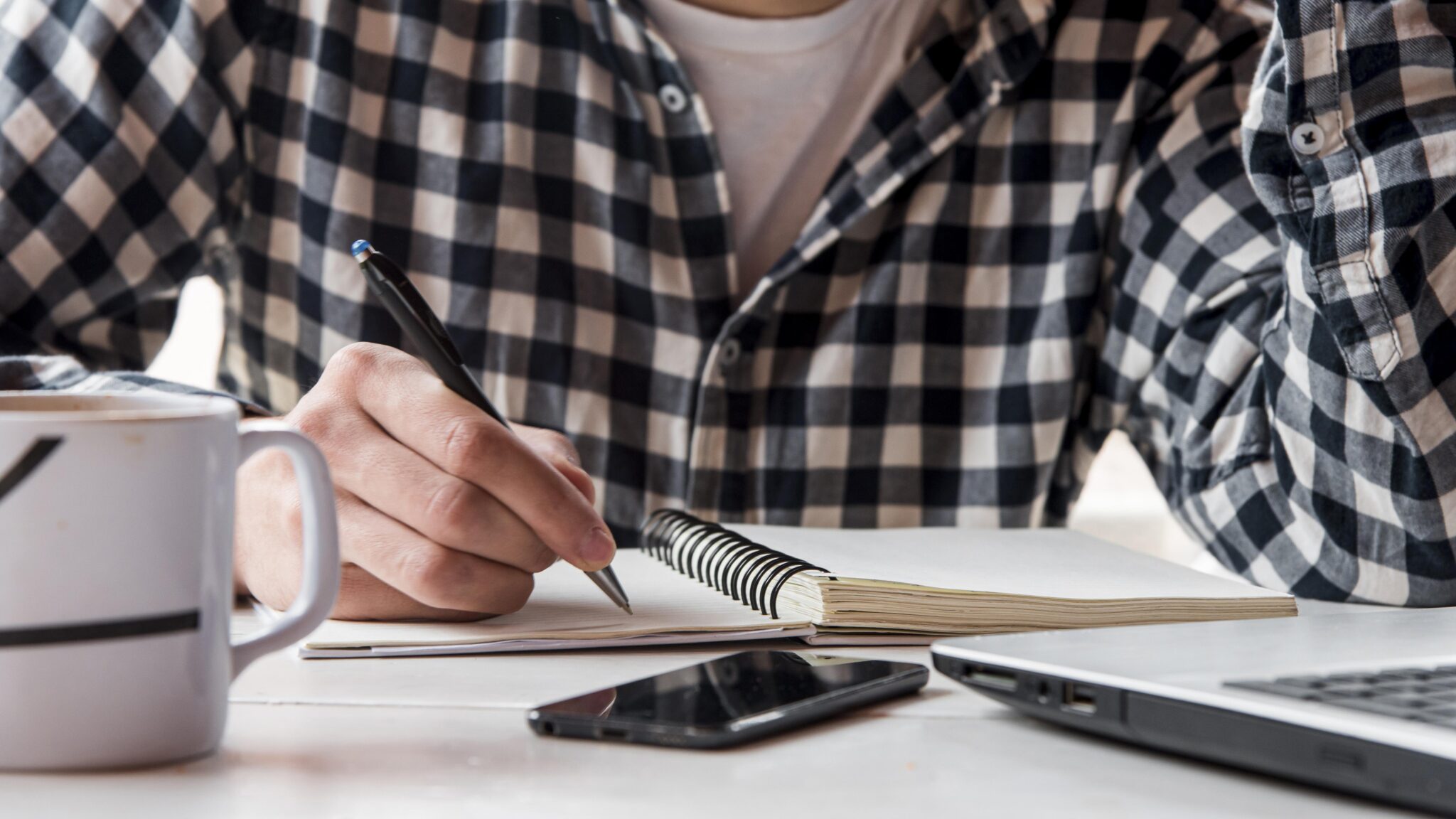A man in a checkered shirt writing New Year's resolutions for his mental health in a notebook