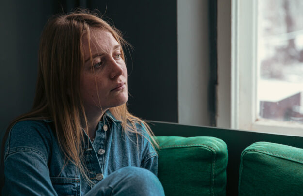 A cute young woman is sitting on the sofa by the window.