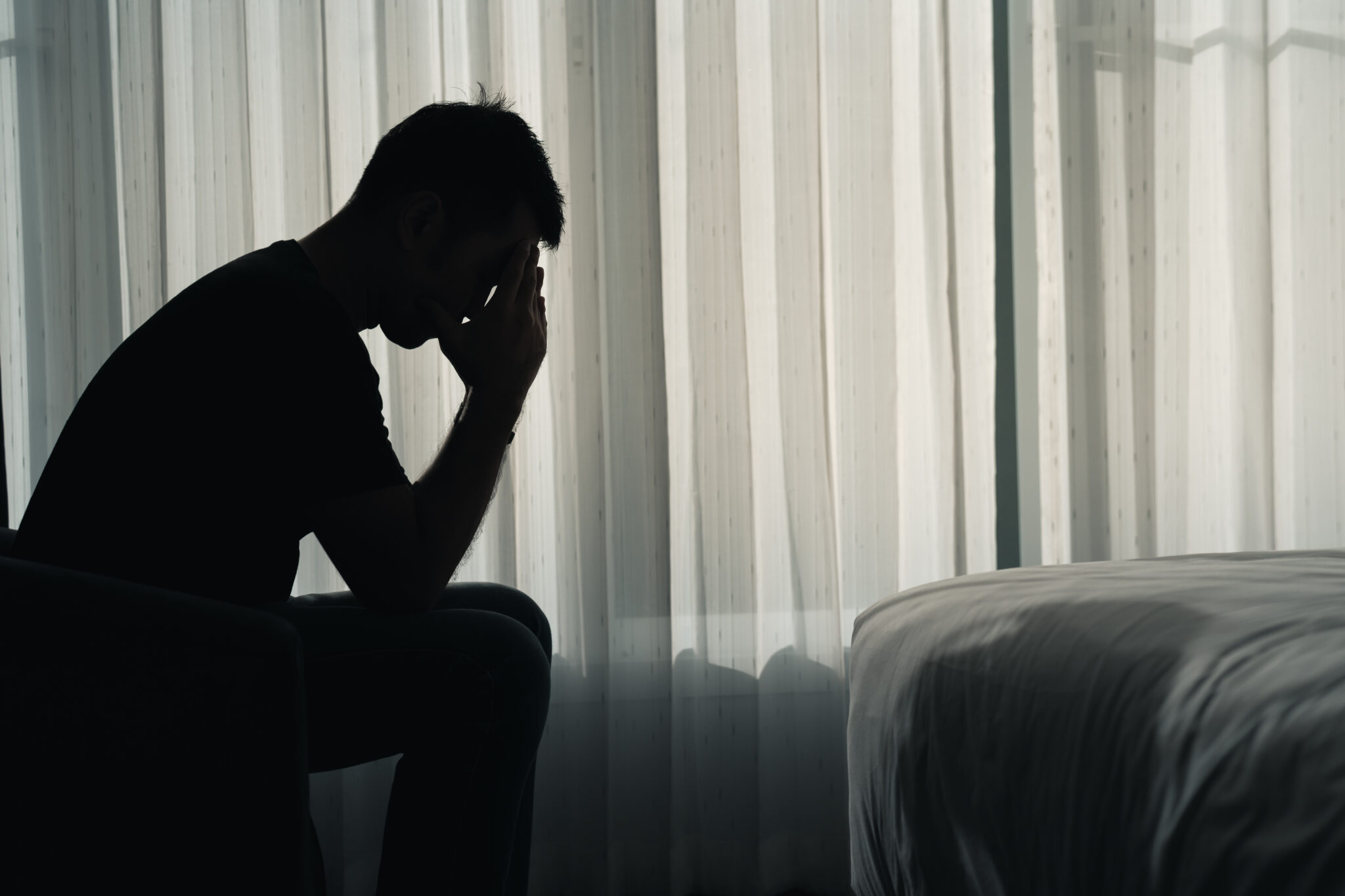 Silhouette depressed man sadly sitting on the bed in the bedroom